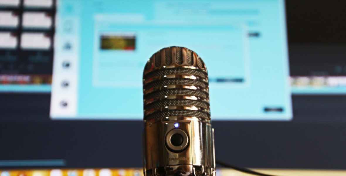 Shiny silver microphone in front of a blurry monitor.