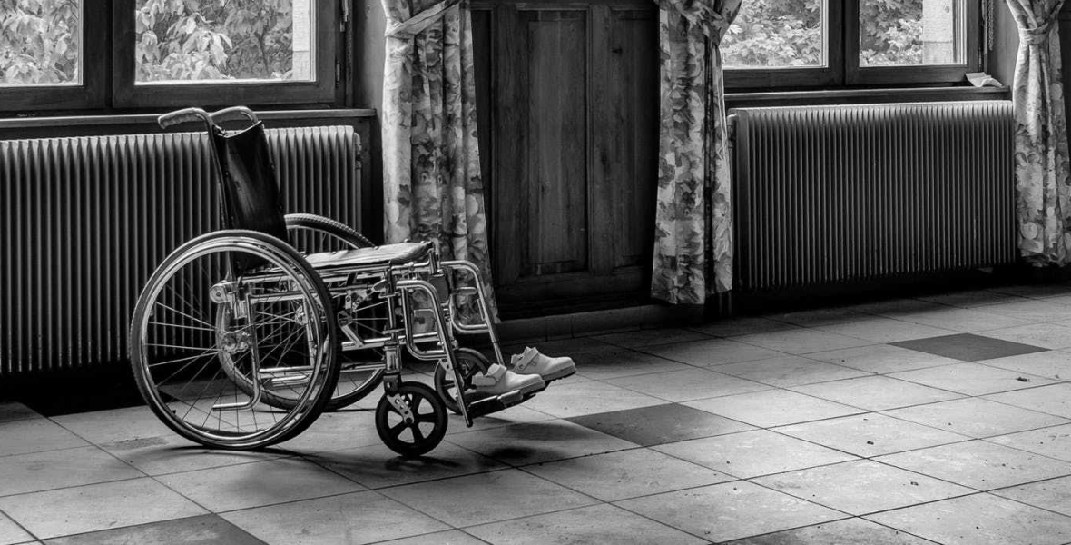 Black and white photo of an empty wheelchair in a bright but empty room.